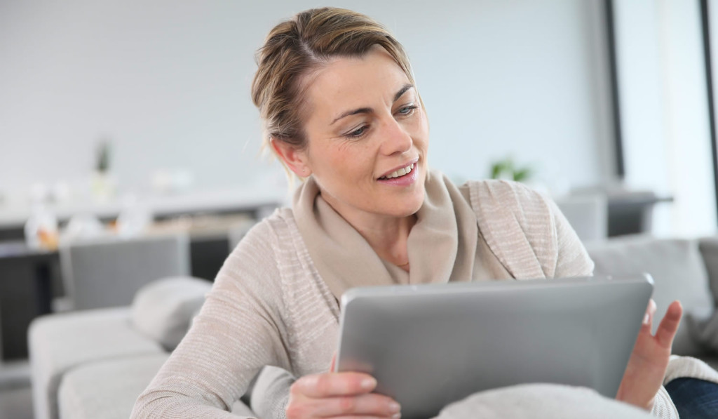 Mature women sitting on the sofa reviewing her tablet news, London City Mortgages