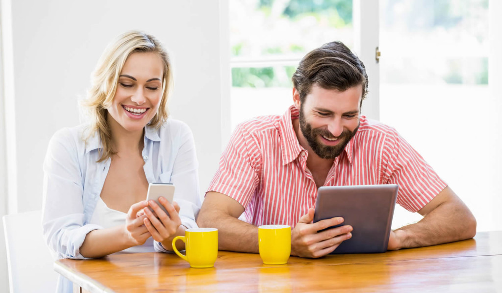 Happy couple using their smartphone and tablet at home, London City Mortgag