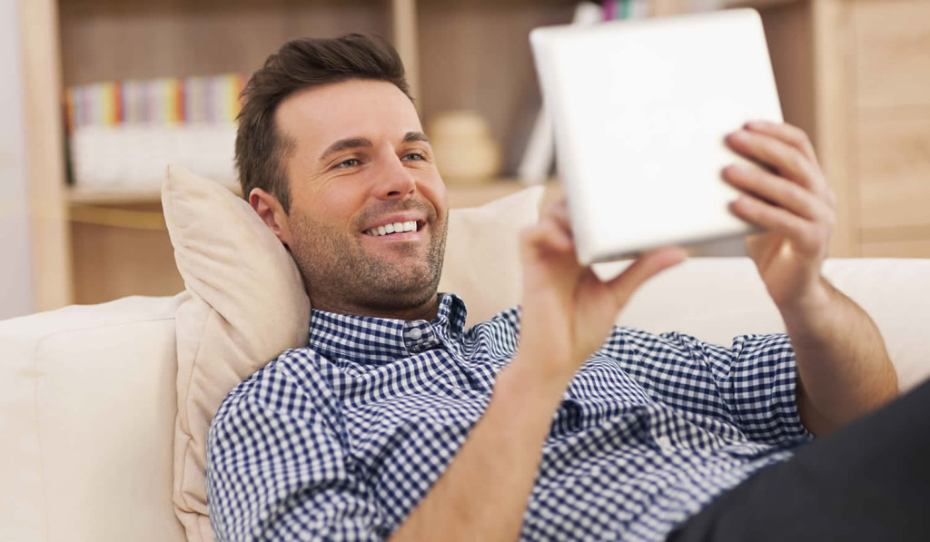 Pleased man relaxing and receiving his latest tablet notices, London City Mortgages