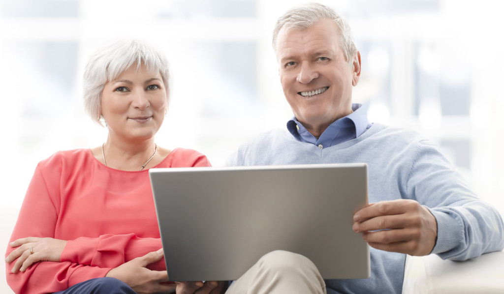 Pleased senior couple on their sofa with laptop updates, London City Mortgages