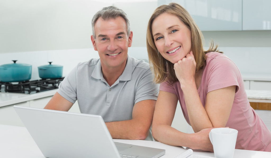 Relaxed older couple in the kitchen receiving laptop updates, London City Mortgages