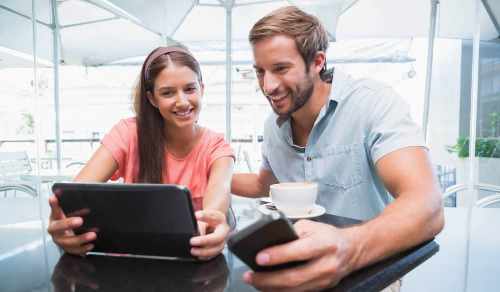 Young couple in a cafe viewing smartphone and tablet updates, London City Mortgages