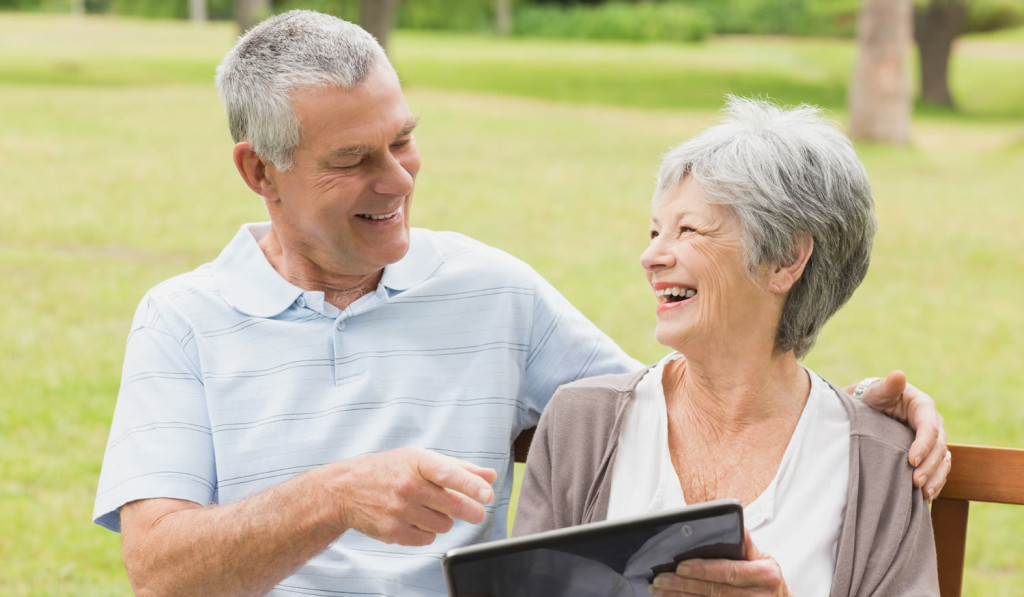 Delighted older couple sitting in park with tablet London City Mortgages